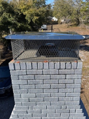 A light gray brick chimney topped with a stainless steel cap and protective wire mesh screen - https://www.juniatachimneyinspectionandrepair.com/