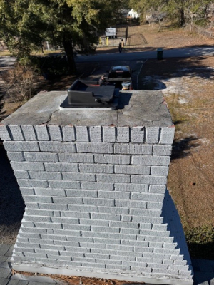 A weathered grey brick chimney features a cracked concrete crown and a black top-sealing damper - https://www.juniatachimneyinspectionandrepair.com/